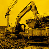 Excavator loading a truck with construction equipment and crane in the background on a yellow-tinted image.
