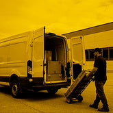 Man loading a dolly with boxes into a white van.